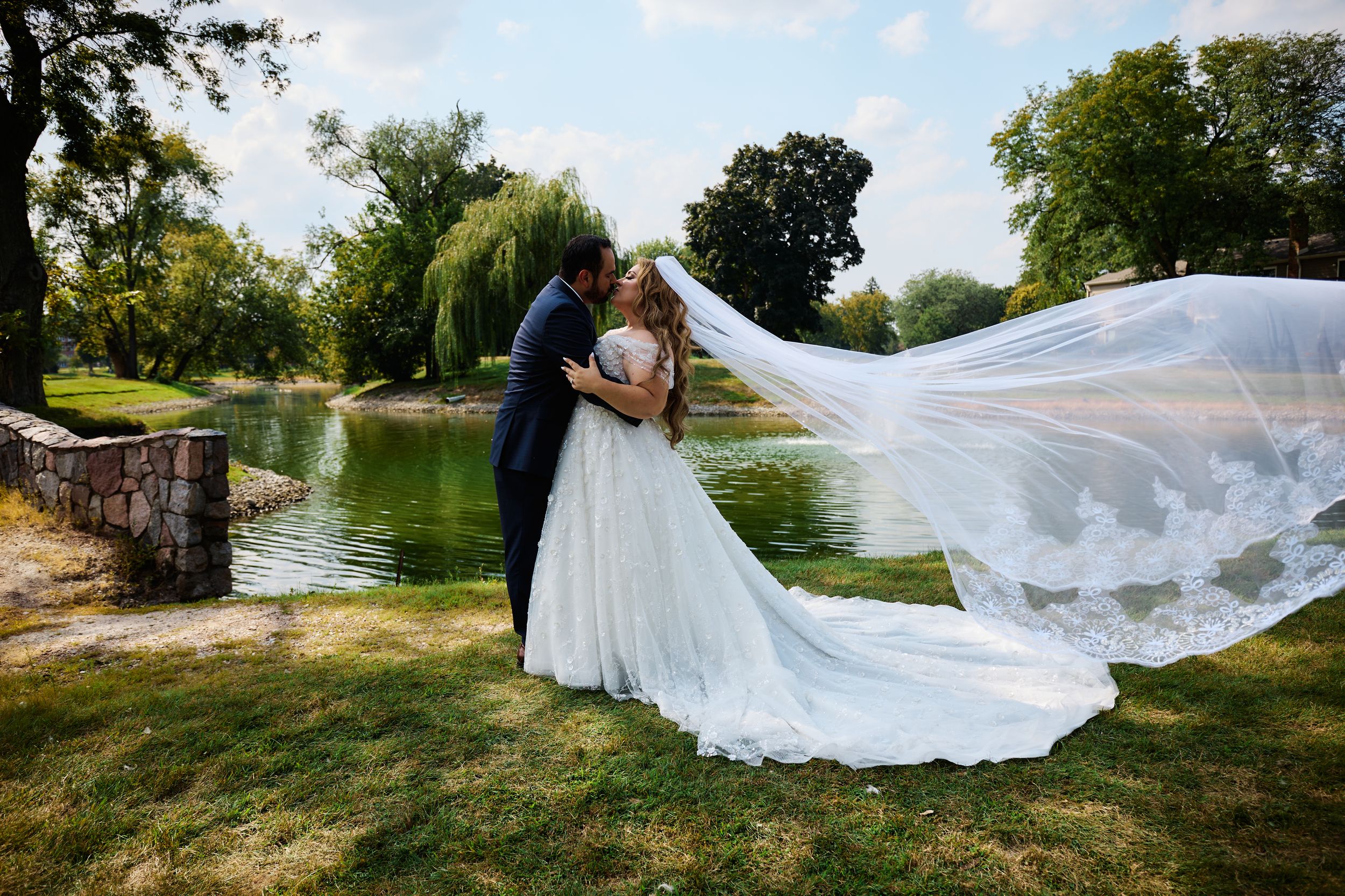 Long flowing white dress and veil billowing dramatically in the wind against a scenic outdoor landscape.