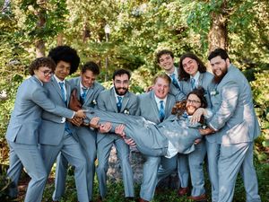 Wedding party in light blue suits poses playfully together for candid photo series in outdoor garden setting.