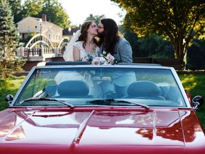 A couple shares a romantic moment in a red vintage convertible car during a sunny outdoor photoshoot.