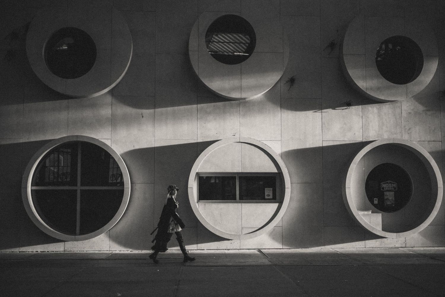 Portrait with the unique architecture of A’DAM Lookout in the background: a woman walking briskly, black and white cinematic shot.