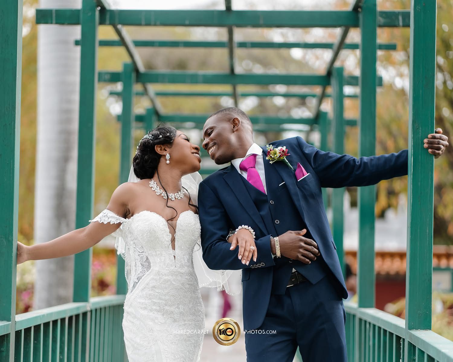 Couple dancing playfully on green-pillared walkway in wedding attire.