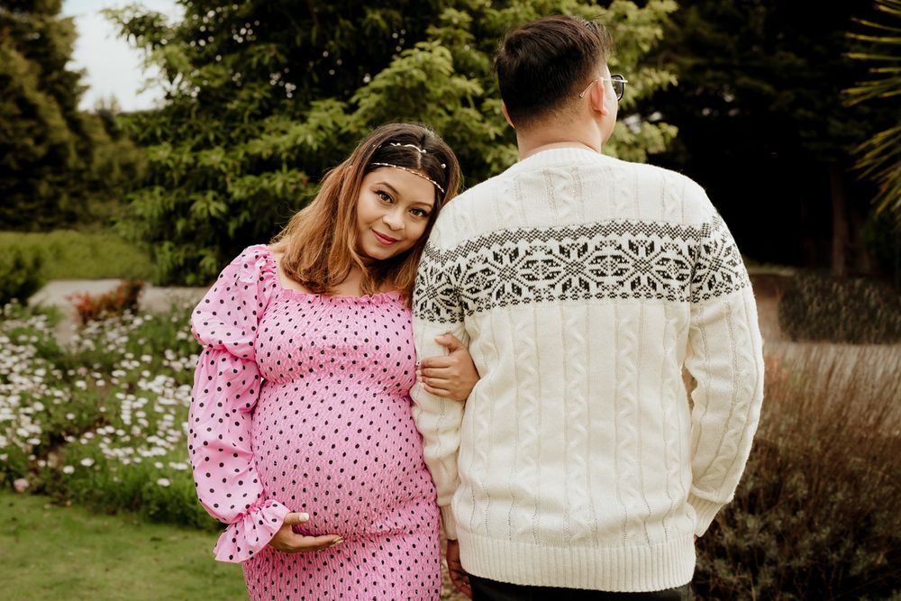 Couple poses in garden, woman wearing pink polka dot dress.
