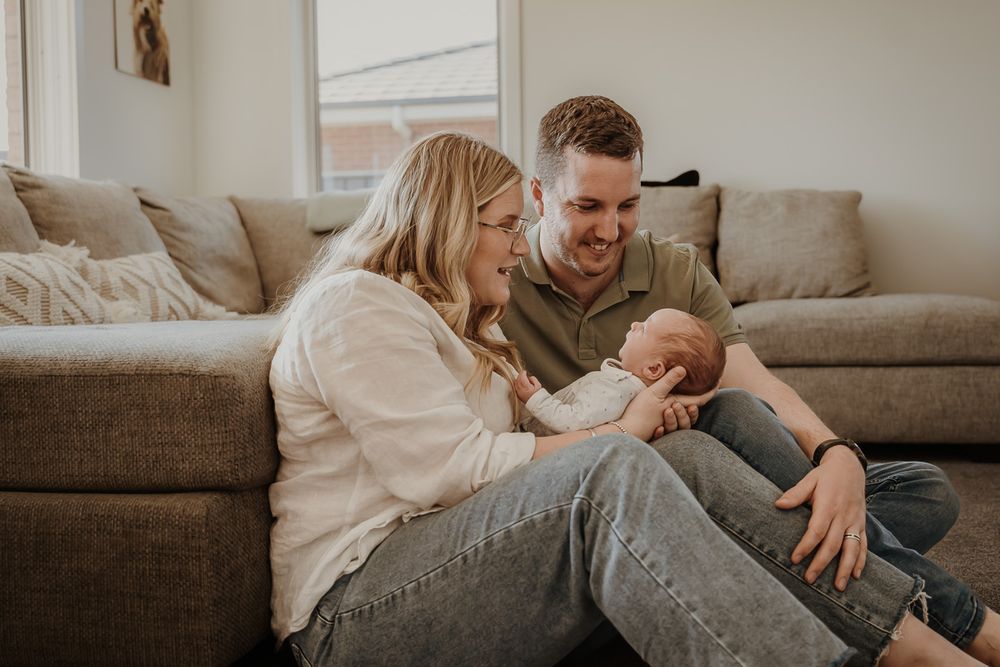 Relaxed couple sitting on gray couch at home with their newborn baby.