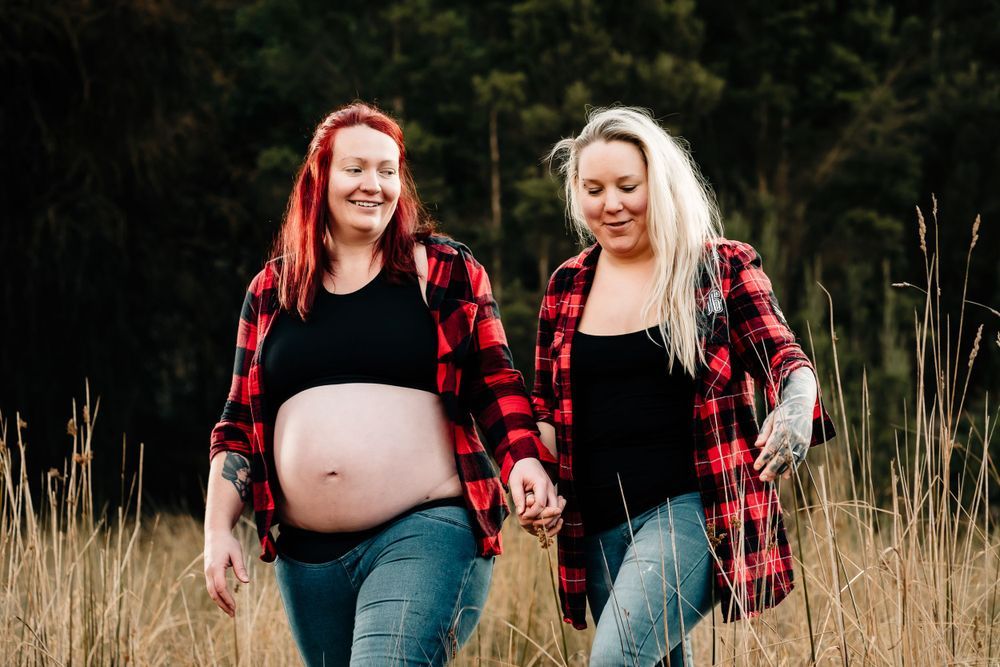 Two women in matching plaid shirts walking through tall grass field.