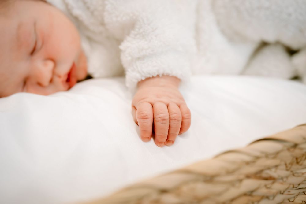 Close up of sleeping baby's tiny hand resting on white bedding.