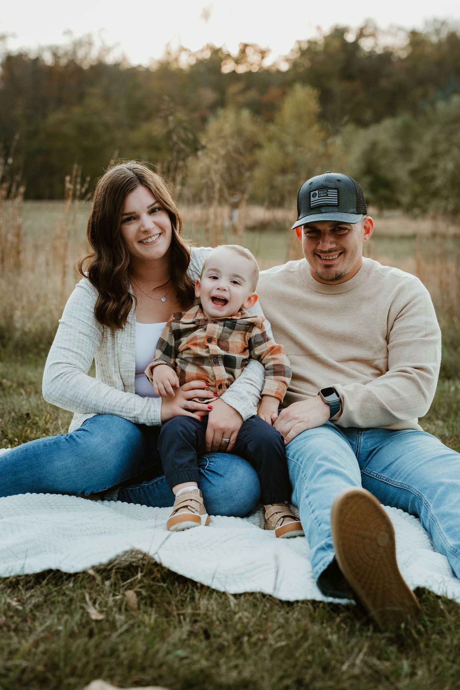 Family sitting on white blanket in field during golden hour.