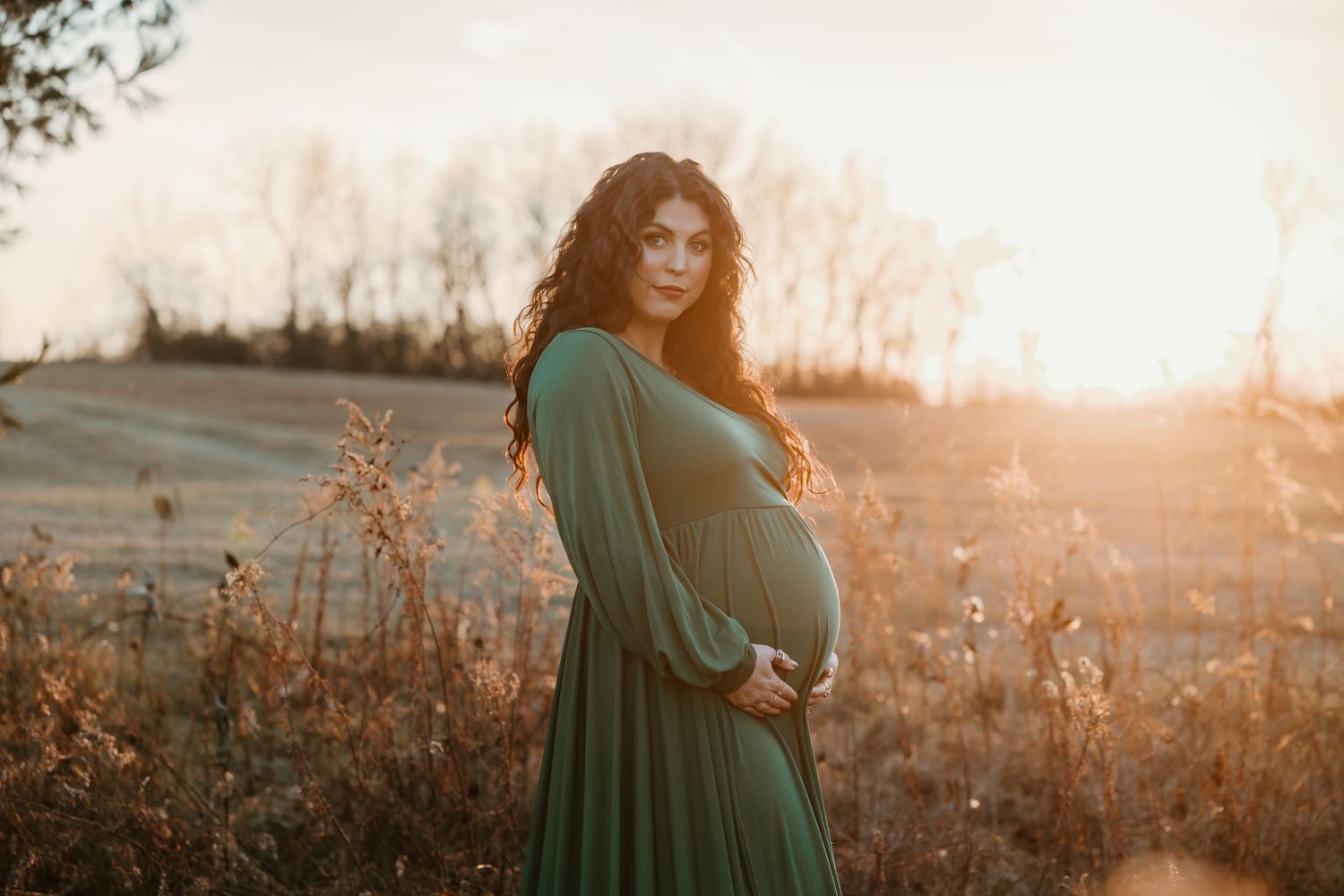 A maternity photoshoot in a field at golden hour featuring a woman in an emerald green dress.