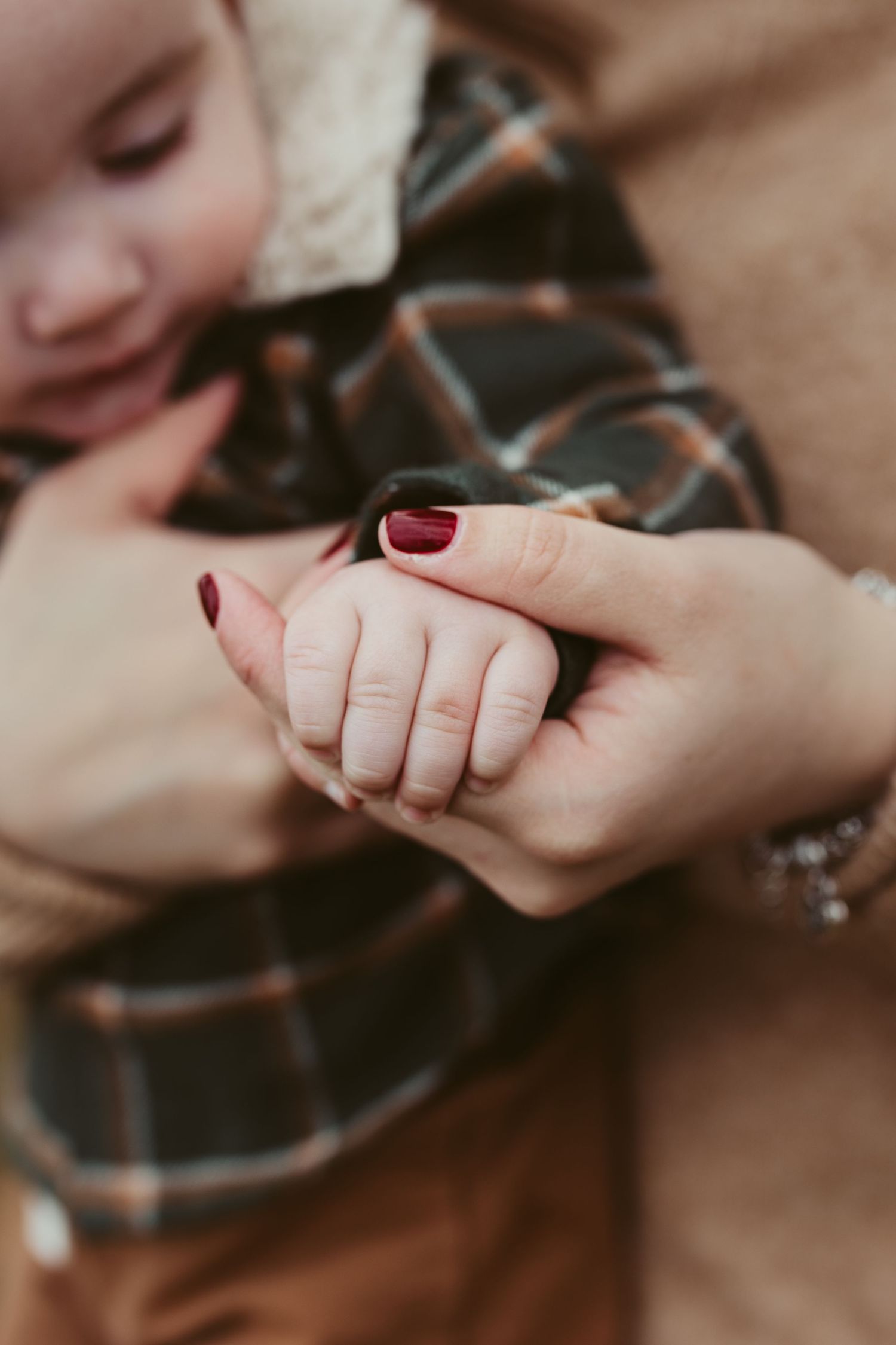 Close-up of small baby hand being held by adult hand with burgundy nail polish.