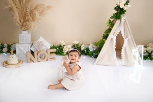 Beautifully styled nursery setup with a white teepee tent, lanterns, and floral decorations against a beige wall.