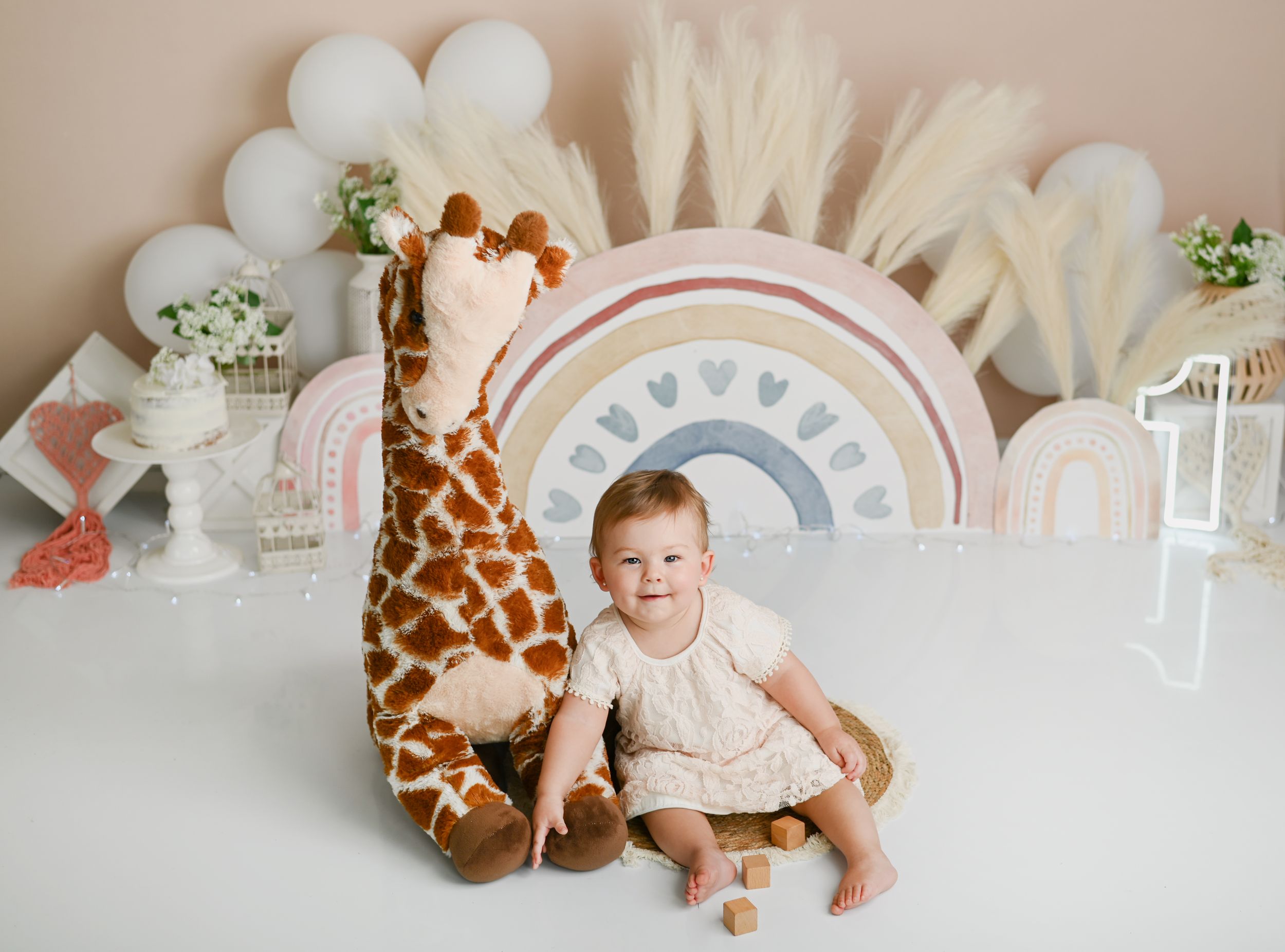 Safari themed photo setup with rainbow arch and large giraffe plush toy.