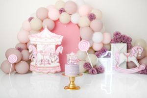 Pink carousel themed first birthday setup with balloon arch and decorative sweets.