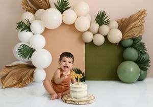 Modern boho first birthday setup with white balloons and palm leaves.