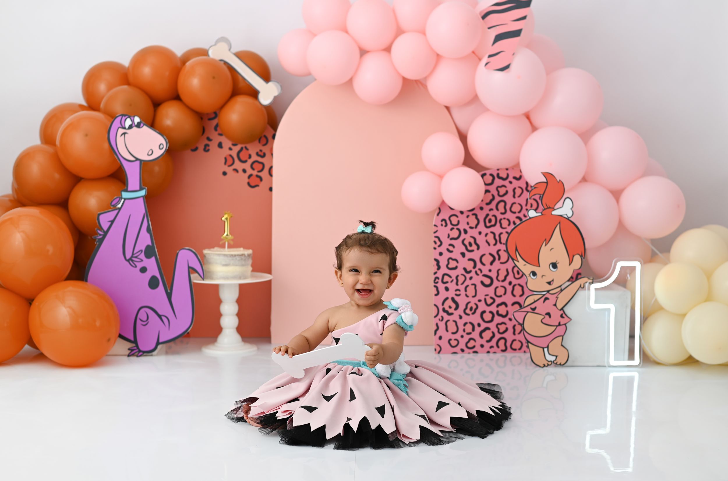 Dinosaur themed birthday setup with pink and orange balloon arch.