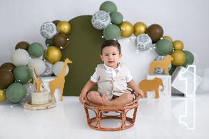 Safari themed birthday setup with balloon arch and wooden animals in earth tones.