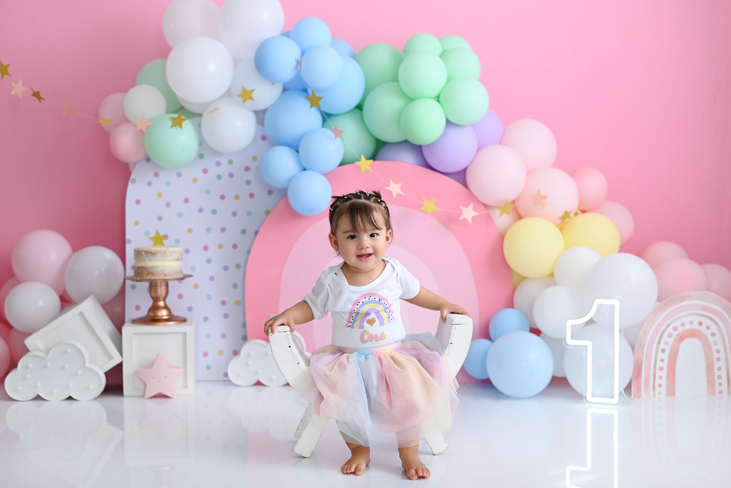 Pastel balloon arch setup with rainbow colors and unicorn decorations for first birthday.