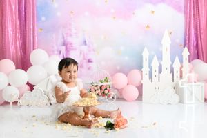 Pink and white themed first birthday cake smash setup with castle backdrop and balloons.