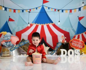 Circus-themed birthday setup with red and blue striped tent backdrop and festive party decorations.