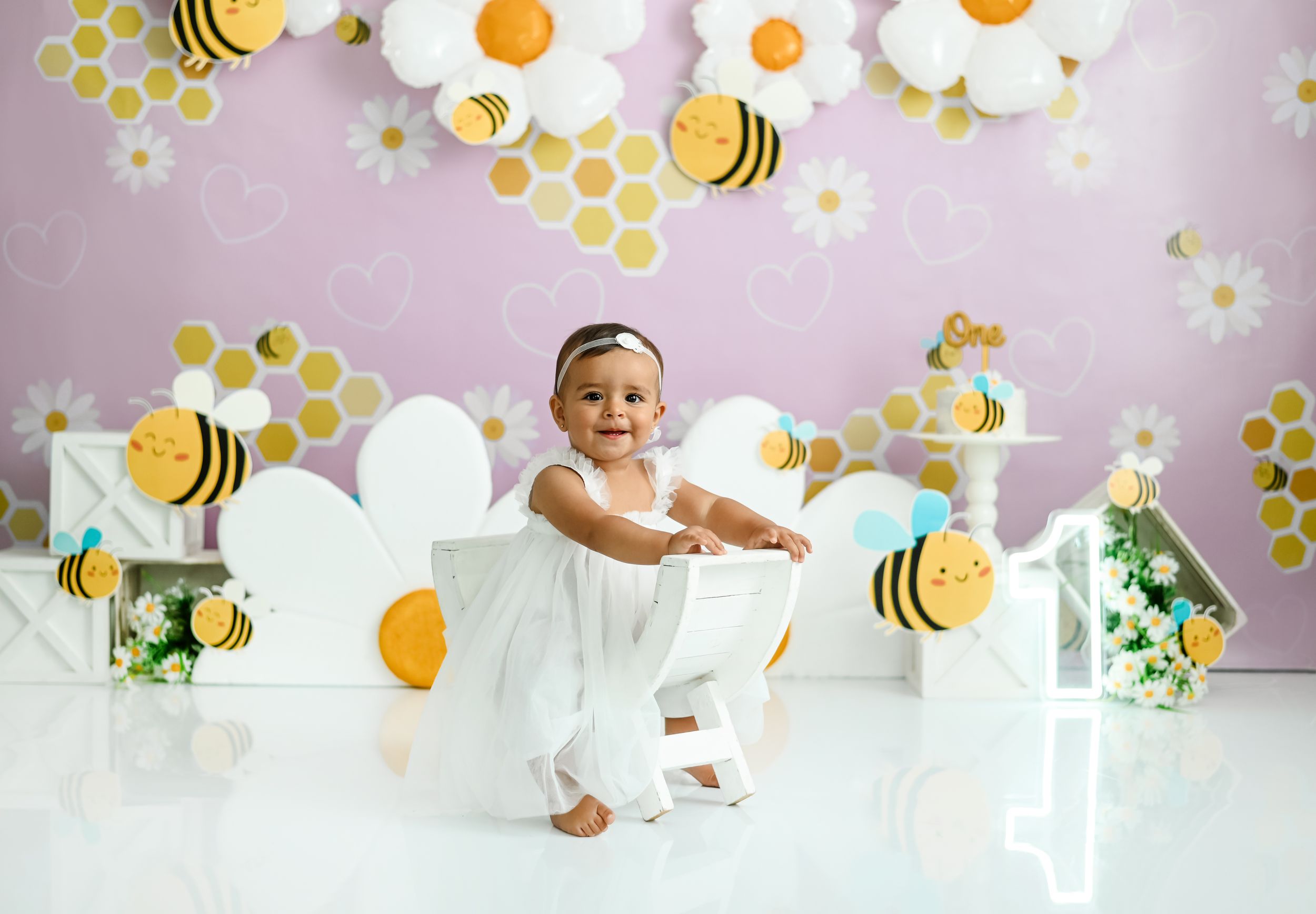 Bee and daisy themed photo setup with honeycomb pattern and balloon decorations.