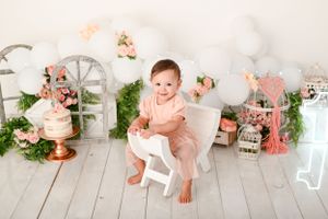 Whimsical garden-themed photography set with floral decorations and white wooden furniture.