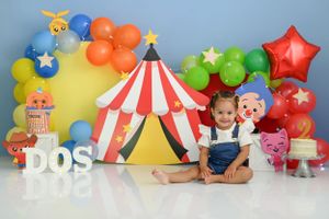 Festive circus-themed birthday setup with red and white striped tent backdrop, colorful balloons, and DOS lettering.