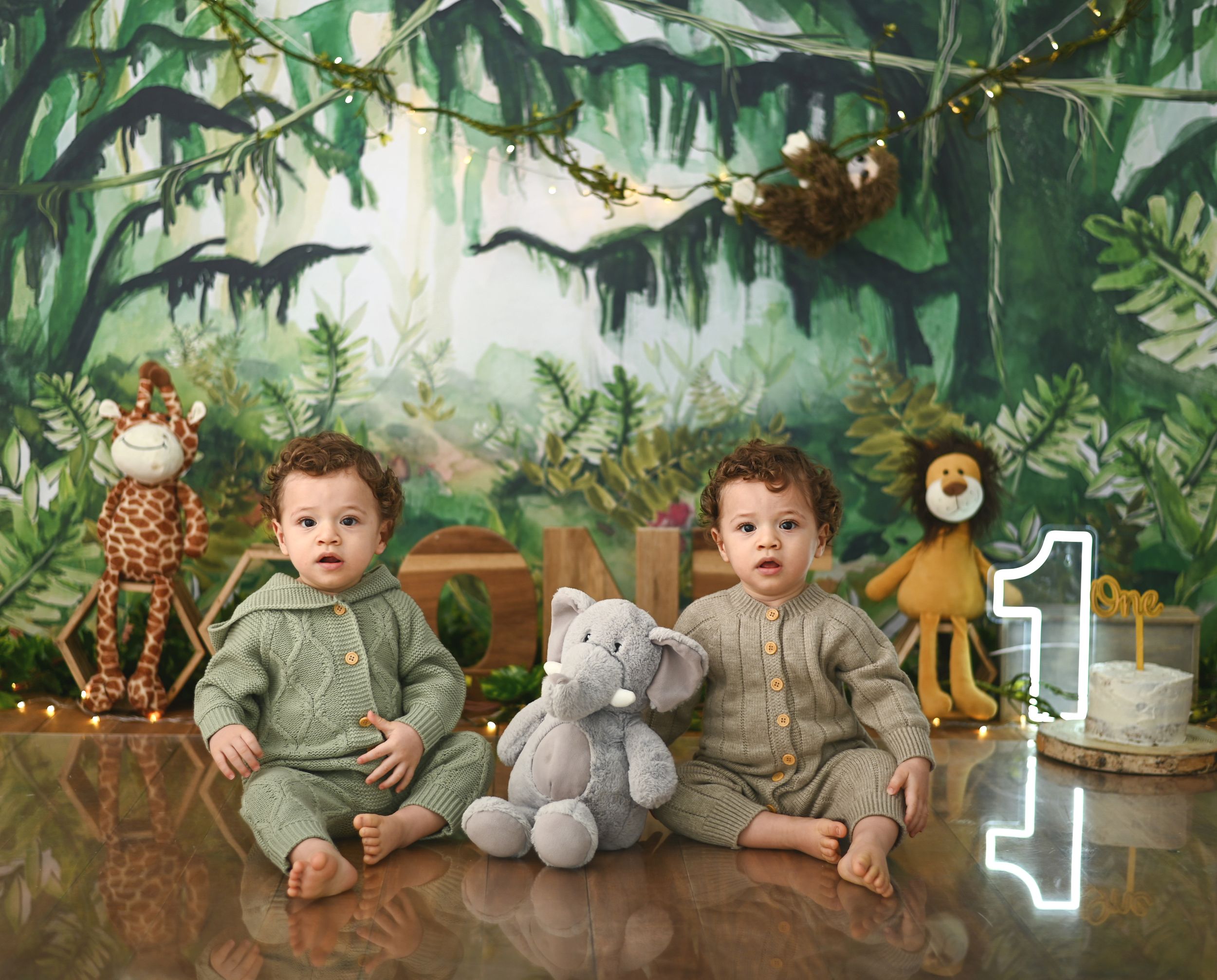 Jungle themed photo setup with twin babies and stuffed animal decorations.