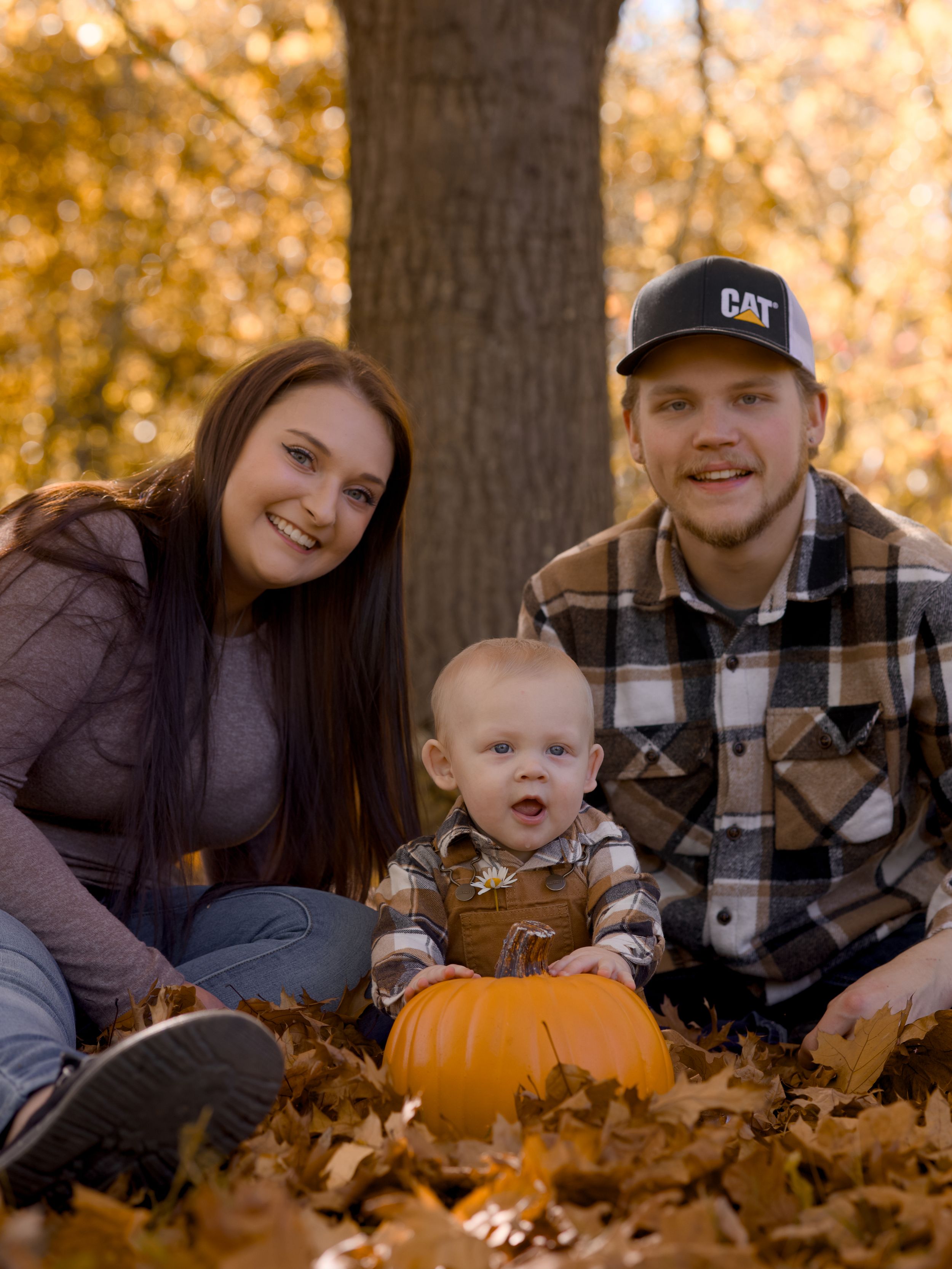 Family poses together with pumpkins and fall leaves during an autumn outdoor photo session.