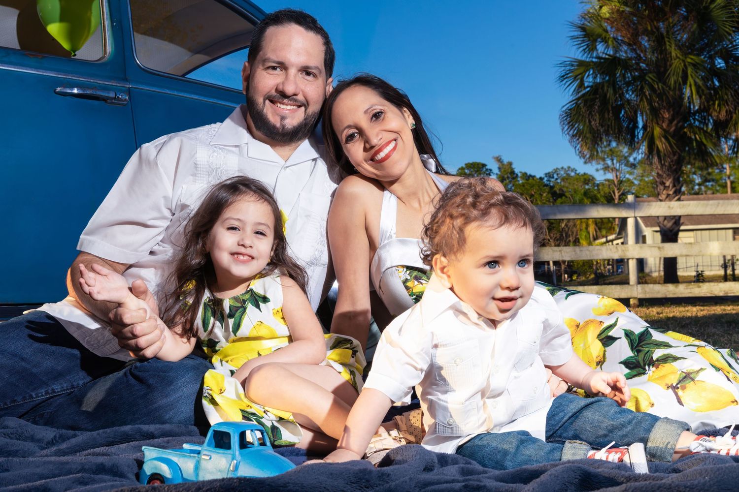 Family relaxing together on blue truck bed with yellow flowers on sunny day.