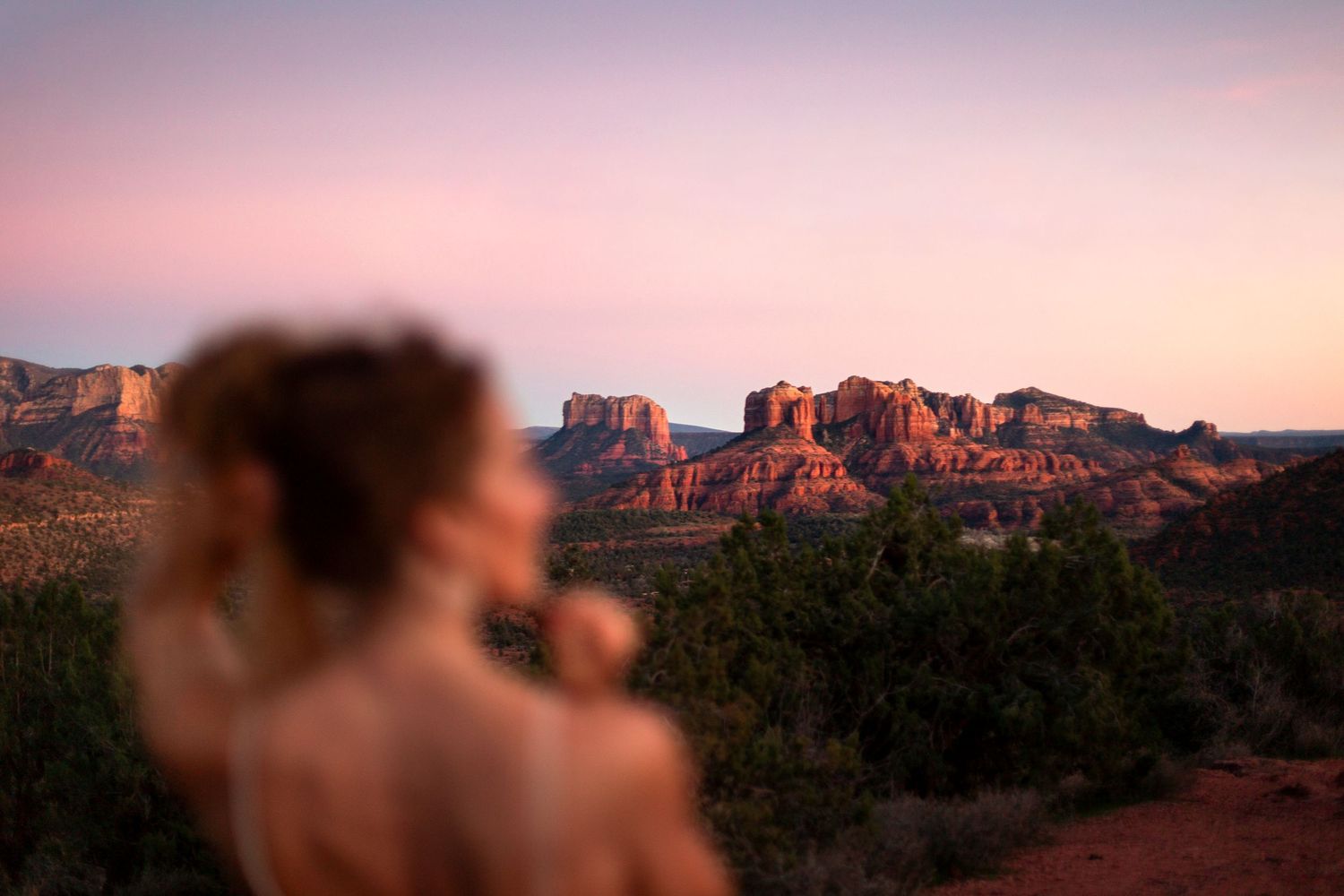 A woman gazes at a stunning pink sunset over the red rock formations of Sedona, Arizona.