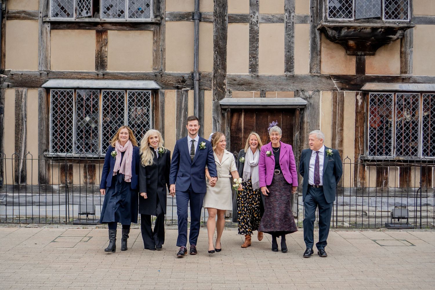 A group of people walking outside a historic Tudor-style building with leaded glass windows and stone architecture.