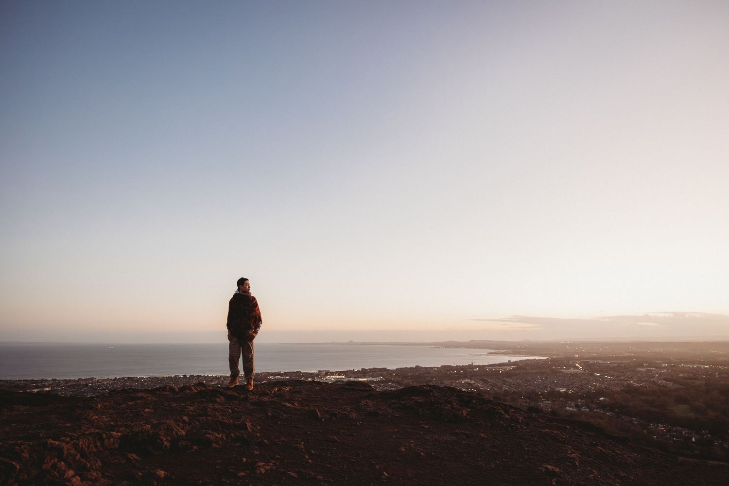 A silhouetted figure stands on a hilltop overlooking a misty coastal landscape at sunset.