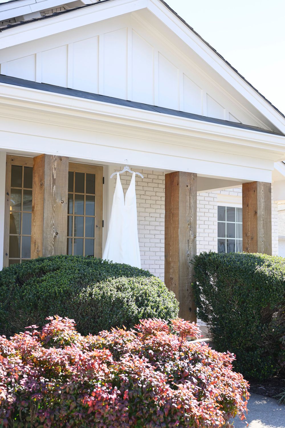 White brick ranch-style house exterior with pink flowering bushes and manicured hedges along the front facade.