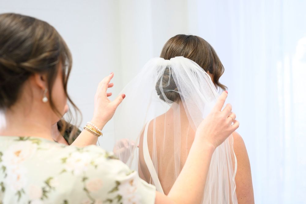 A bride and her bridesmaids raise their hands in celebration during a wedding photoshoot with white curtain backdrop.