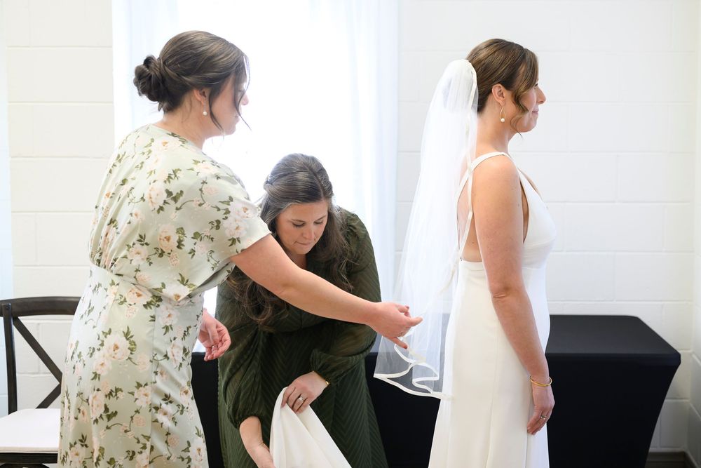 A bride gets help with her wedding dress fitting and adjustments during a pre-wedding preparation moment.