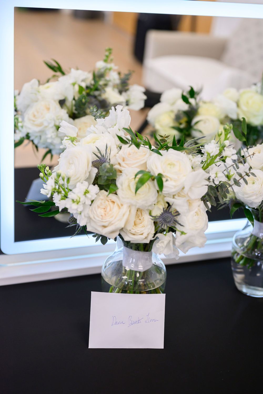 Elegant white rose and greenery centerpiece arrangements in glass vases displayed on a table at a formal event.