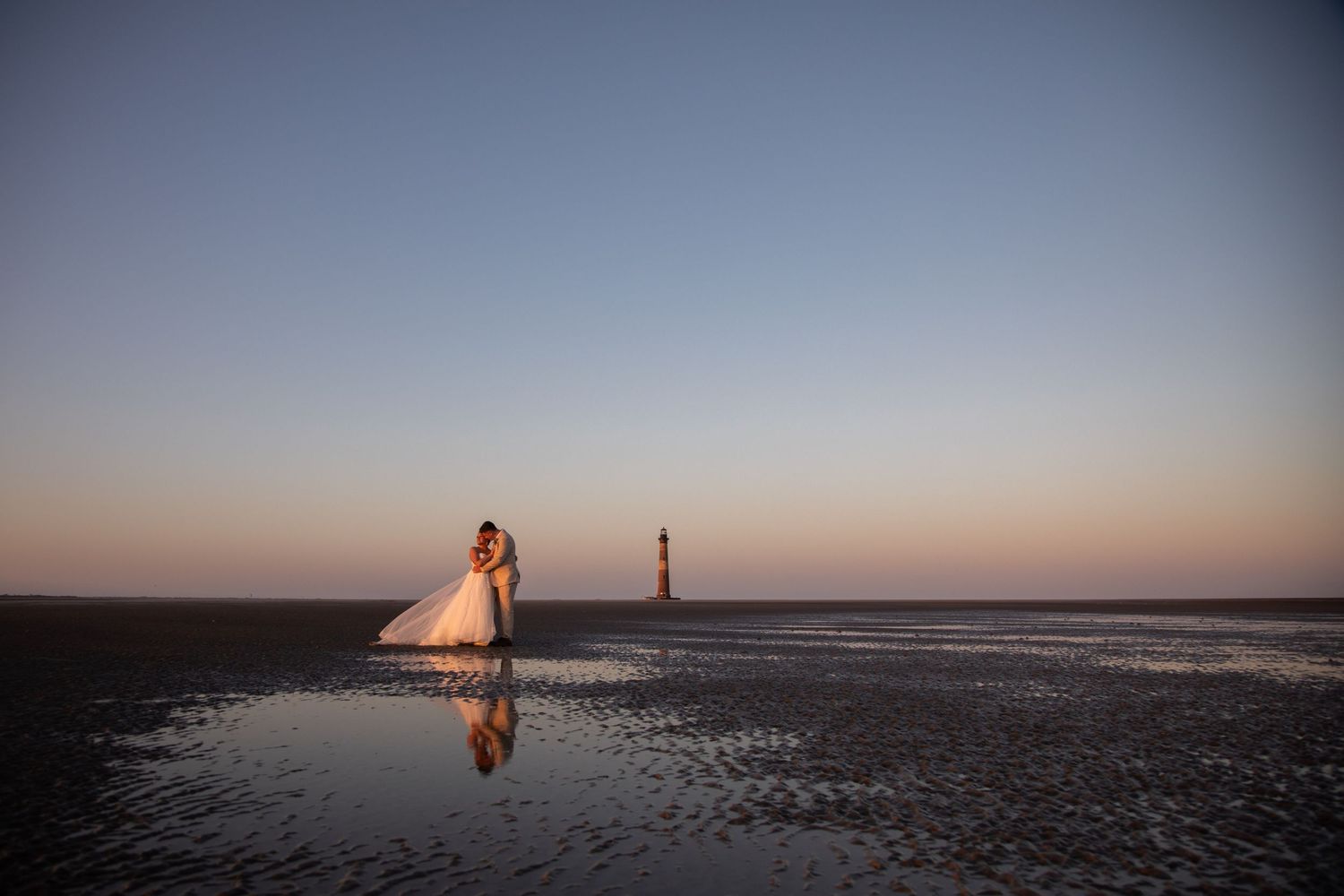 A couple in wedding attire embraces in a golden field at sunset during their romantic outdoor photoshoot.