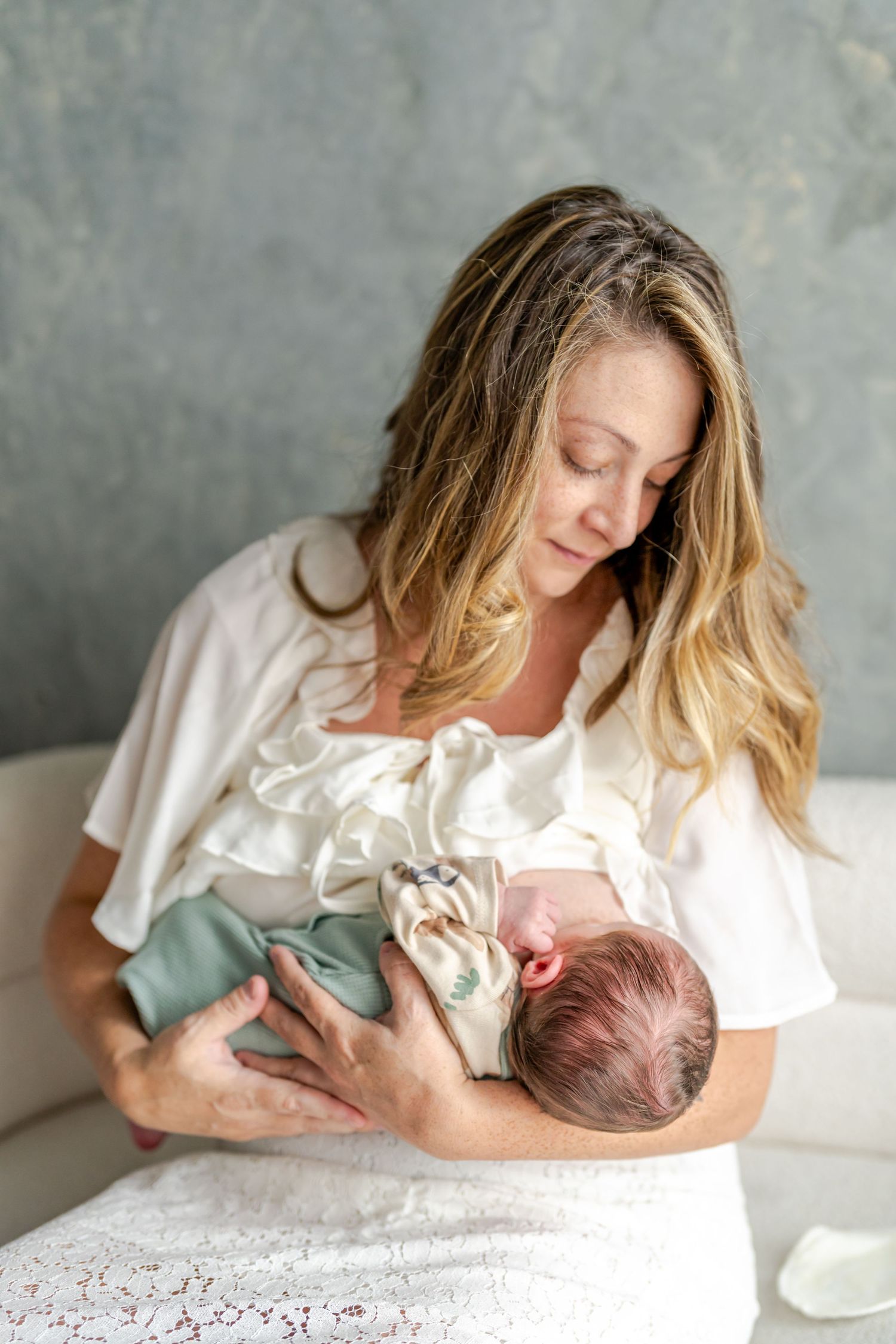 A mother in white clothing tenderly holds and gazes at her newborn baby in soft natural lighting.