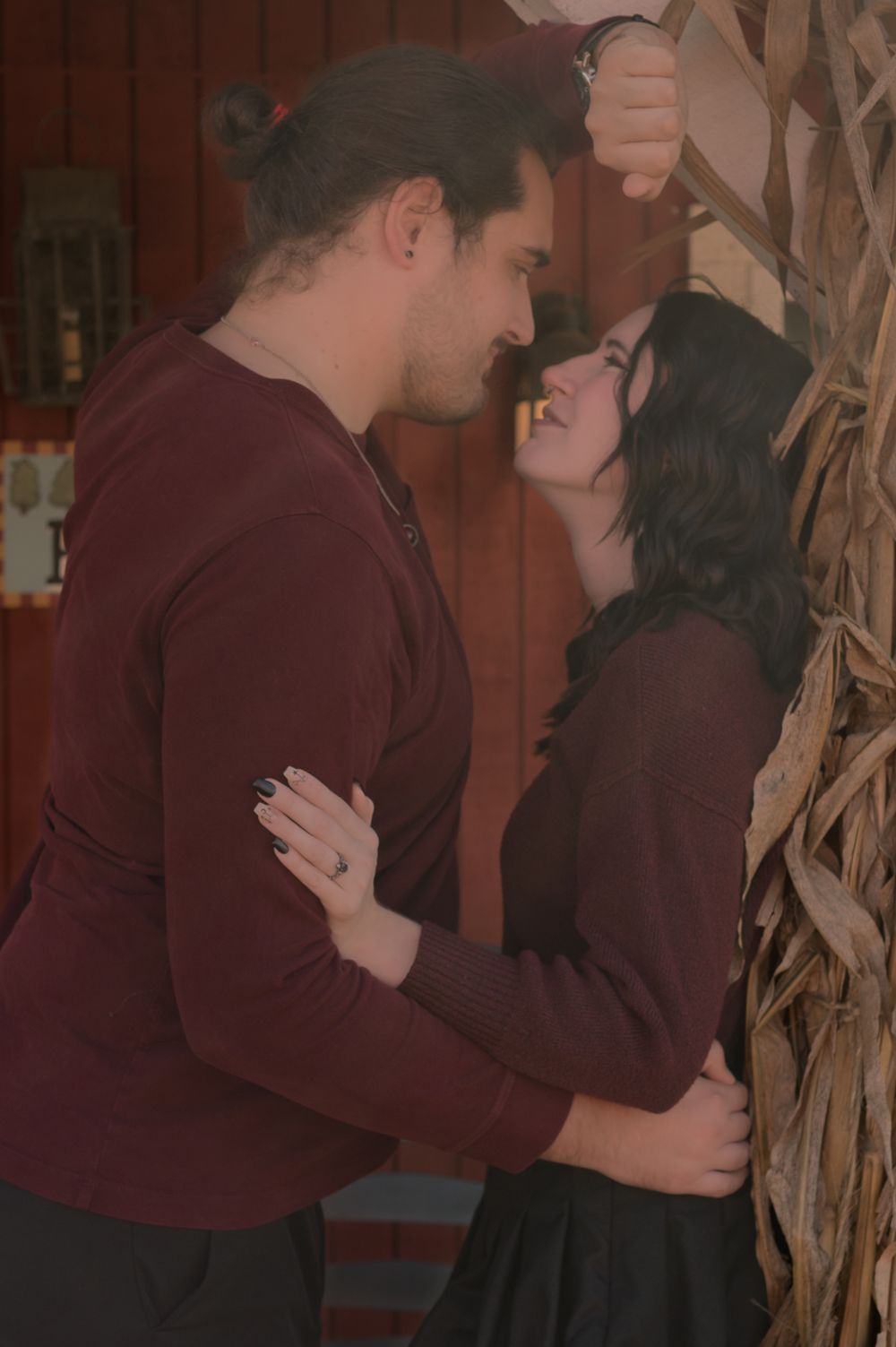 Romantic couple in matching burgundy outfits sharing an intimate moment near rustic decor.