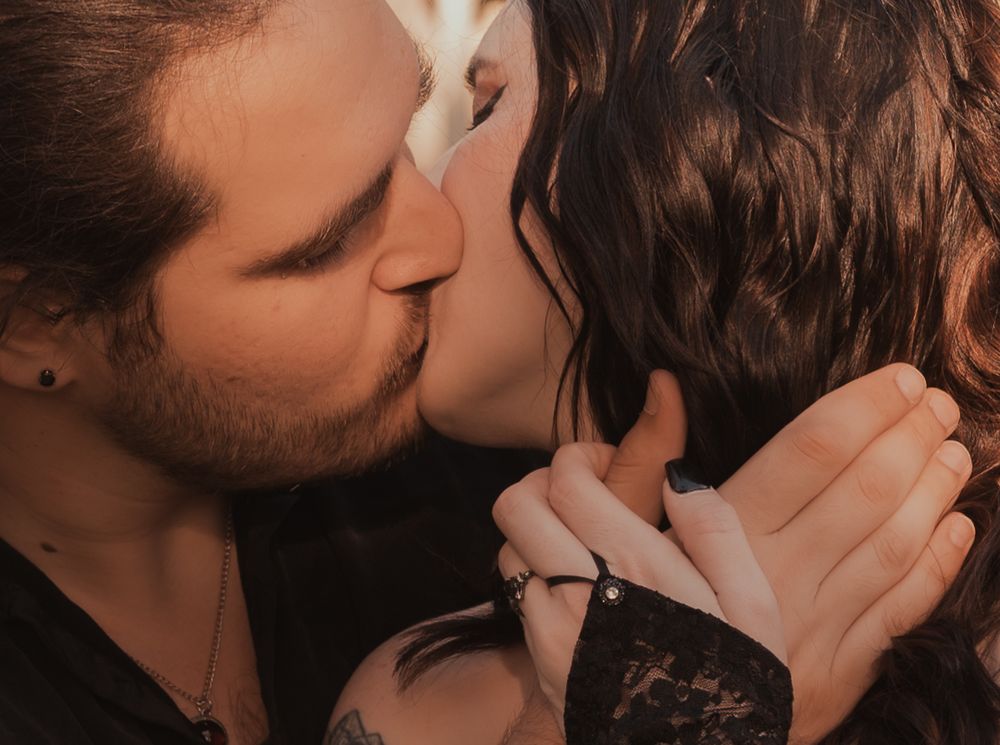 A couple shares a romantic kiss, with the man having light stubble and the woman with dark wavy hair.