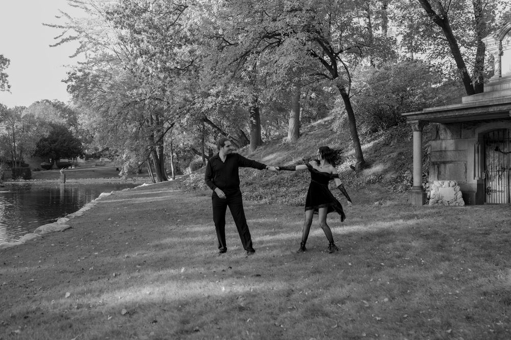 Black and white photo of a couple dancing outdoors near a pond surrounded by trees.