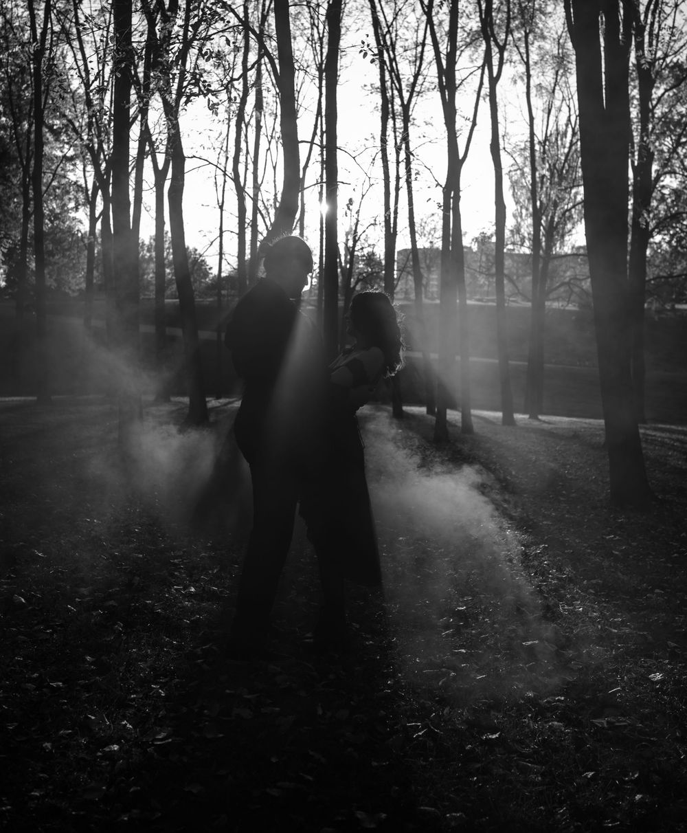 Dramatic black and white silhouette of a person standing in misty woods with sunlight rays filtering through bare trees.