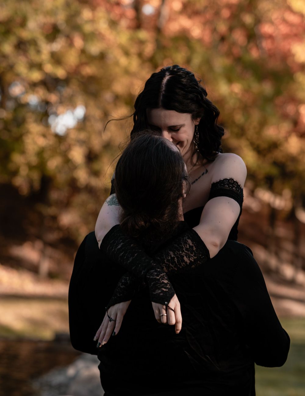 Two people sharing a joyful embrace outdoors with colorful fall foliage in the background.