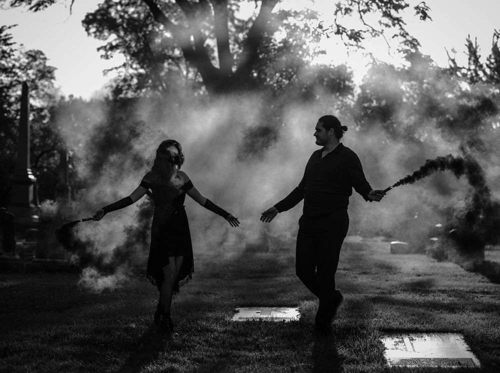 Black and white photo of couple holding smoke bombs in a dramatic outdoor setting.