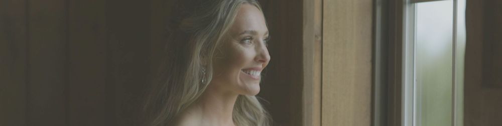 A person smiles warmly while seated in front of a window with natural light streaming in.