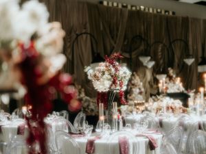 Elegant wedding reception tables decorated with burgundy floral centerpieces and glowing candles in a rustic wooden venue.
