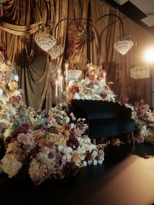 Elegant wedding venue with crystal chandeliers and luxurious floral arrangements draped across dark curtained walls.