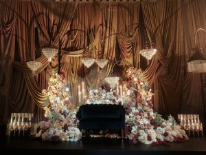 Elegant wedding reception ballroom with crystal chandeliers and draped fabric adorned with lush floral arrangements.