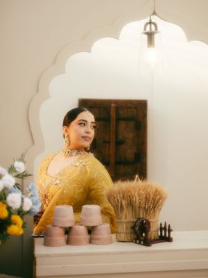 A rustic wedding display with pink dessert stands, dried wheat stalks, and floral arrangements against a white wall.