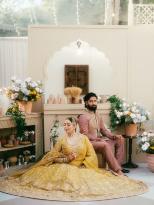 Couple poses in traditional yellow and pink wedding attire surrounded by white floral arrangements.