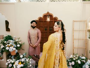 Wedding photoshoot featuring yellow bridal lehenga and pink groom's outfit in white studio setting.