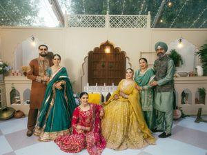 Wedding party gathered in an indoor venue wearing traditional Indian attire in emerald, yellow and red colors.